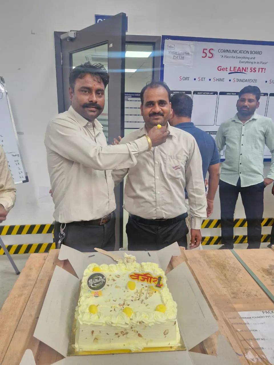 Colleagues cutting a cake in front of the 5S operations board