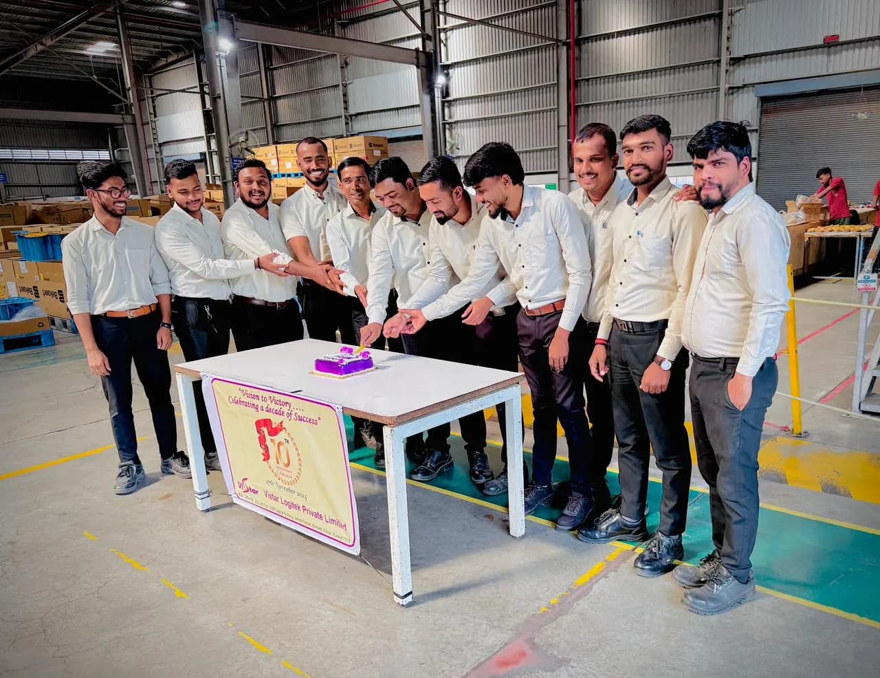 Warehouse colleagues assembled around a celebration table between racking aisles